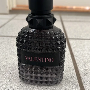 Valentino parfym med edgy design - Snygg parfym från Valentino i en mörk, cool flaska med nitar. Perfekt för dig som gillar att sticka ut och vill ha en lyxig touch i din samling. Volym och ingredienser syns ej på bilderna.