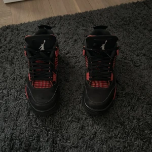 Jordan 4 red thunder - Säljer ett par Nike Air Jordan 4 sneakers i svart och rött med klassisk Jumpman-logga på plösen. Skorna har snygga detaljer med meshpaneler, snörning och en robust sula. Perfekta för dig som vill sticka ut med en ikonisk och sportig look. Storlek 41