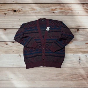 Mönstrad kofta från Filati i vinrött - Retro kofta från Filati i vinröda och mörkblå toner med geometriskt mönster. Koftan har v-ringning, knappar framtill och ribbade muddar. Perfekt för dig som gillar vintagevibbar och vill sticka ut med en unik look.