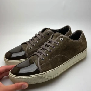 Bruna lanvins captoes mocka med gläns - Snygga bruna sneakers från Lanvin med ovandel i mocka och lackad tå i mörkbrunt. Skorna har beige sula, rund tå och klassisk snörning. Perfekta för dig som gillar stilrena och exklusiva detaljer.