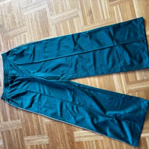 Turkosa wide byxor från Divided - Säljer ett par turkosa wide byxor från Divided med resår i midjan. Byxorna har en avslappnad passform och är tillverkade i ett mjukt syntetmaterial som känns skönt mot huden. Perfekta för en chill och trendig look.