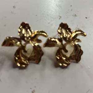 Guldiga blommiga örhängen - Unika örhängen i guldig metall med ett snyggt blommigt formspråk. De har en cool, skulptural design som verkligen sticker ut och ger en lyxig känsla. Perfekta för dig som vill ha något annorlunda och trendigt i smyckeslådan.