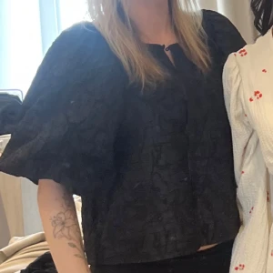 Svart blus med puffärm från Gina Tricot - Säljer en svart blus från Gina Tricot med cool struktur i tyget och stora puffärmar. Blusen har rund halsringning och knäppning framtill. Den boxiga passformen och det unika materialet gör den till ett statement-plagg. Perfekt för dig som vill sticka ut lite extra.