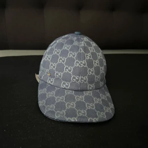 Gucci keps - Snygg blå keps från Gucci med ikoniskt GG-mönster över hela kepsen. Tillverkad i bomullstyg med klassisk böjd skärm och justerbar baksida. Perfekt för dig som vill sticka ut med en exklusiv accessoar kespen är i ny sick 