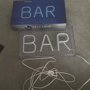 Veli Line Neon Bar Skylt - Stilren neonlampa med texten 'BAR' från Veli Line Denmark. Perfekt för hemmabaren eller festen. USB-anslutning, levereras i originalförpackning. Lampan är i ny skick utan synliga skador eller slitage.