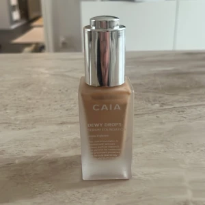 CAIA Dewy Drops Serum Foundation - Säljer en CAIA Dewy Drops Serum Foundation i en snygg frostad glasflaska med silvrig pump. Färgen är medium beige 20W med varm underton och ger en fräsch, glowig finish. Perfekt för dig som vill ha en naturlig look med lyster. Enkel att applicera tack vare smidig pump. Denna är nästan helt oanvänd!!