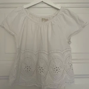 Vit blus med broderi - Superfin vit blus med korta ärmar och broderade hålmönster längst ner. Blusen har en lös passform och elastisk halsringning som ger en avslappnad vibe. Perfekt för varma dagar och enkel att matcha med jeans eller shorts. Har använts några gånger så säljer för 189, nypris 300 💗