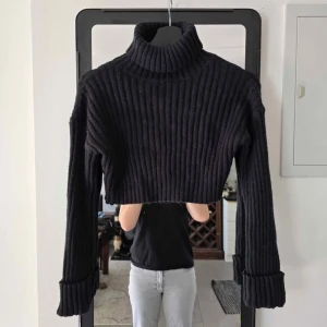 Svart croppad polotröja, ribbstickad - Säljer en svart croppad polotröja med bred ribbstickning och uppvikta ärmslut. Tröjan har hög polokrage och är långärmad, perfekt för att skapa en trendig lager-på-lager-look.