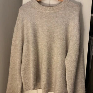 Beige stickad tröja från Gina tricot  - Mysig beige stickad tröja med rund halsringning och långa ärmar. Tröjan har en avslappnad passform och ribbade muddar vid ärmslut och nederkant. Perfekt för lager-på-lager under kyliga dagar.
