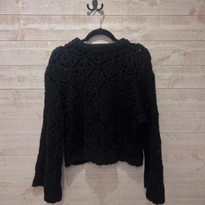 Svart stickad tröja från Zara - Säljer en svart stickad tröja från Zara med snyggt virkat mönster och lång ärm. Tröjan har en loose fit och är perfekt för lager-på-lager-stil. Superfin till både jeans och kjol för en trendig look.