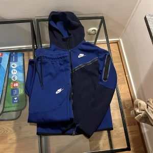 Nike tech fleece tracksuit byxa (s) tröja (xs) - Nike hoodie i marinblått med hel dragkedja och huva. Snyggt sportig design med svarta detaljer och vit Nike-logga på bröstet. Tillverkad i mjukt material, perfekt för chill eller träning. Långa ärmar och praktiska fickor med dragkedja.Änvänd 1-3 gånger tracksuiten är i extremt bra skick köpte den för 2200 kr och den säljs inte längre i affär den är extremt sällsynt jag säljer den för 850 men den kan vidare säljas för mycket dyrare eftersom den är så sällsynt.