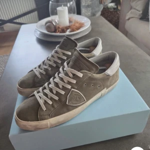 Philippe Model  - Snygga sneakers från Philippe Model i olivgrön mocka med vita detaljer och snörning. Skorna har en klassisk låg profil, vit sula och rund tå. Bakpartiet är vitt med logga och sidorna har den ikoniska skölden. Perfekta för en stilren och avslappnad look. Inga defekter förutom lite inne vid sulan som inte märks när man har på dom elelr syns 9/10 skick😁 priset är inte hugget i sten! Har ni frågor eller funderingar är det bara att höra av er!  😁
