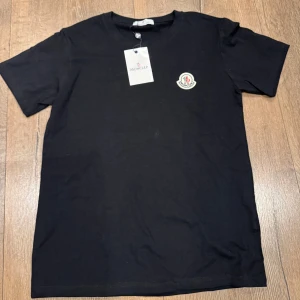 Svart Moncler t-shirt i S - Svart t-shirt från Moncler i 100% bomull med klassisk passform. T-shirten har rund halsringning, korta ärmar och Moncler-logga broderad på bröstet. Perfekt basic med exklusiv känsla och snygg detalj.