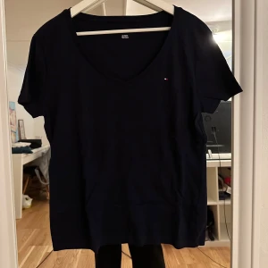 Svart v-ringad t-shirt Tommy Hilfiger - Svart t-shirt från Tommy Hilfiger med v-ringning och liten broderad logga på bröstet. Klassisk passform och korta ärmar, tillverkad i mjuk bomull. Perfekt för en clean och stilren look.