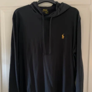 Svart tunn hoodie från Polo Ralph Lauren - En Svart tunn luvtröja från Polo Ralph Lauren med klassisk gul broderad logga på bröstet. Tröjan har huva med snörning och är tillverkad i mjuk bomull. Långärmad och stilren modell som passar perfekt till allt. Storlek S. Skriv till mig vid minsta fråga eller fundering! 