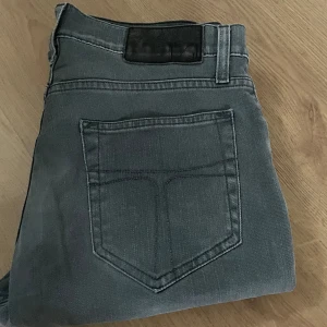 Grå jeans från tiger of sweden - Snygga grå jeans från tiger of sweden med klassisk femficksdesign och svarta detaljer på bakfickan. Jeansen har raka ben och normal passform, tillverkade i mjukt jeanstyg som är sköna att bära hela dagen. Riktigt feta, passar till det mesta! Storlek 28/32. Hör av dig vid fundering! Kan gå ner i pris vid snabbt köp!