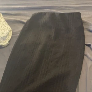 Svart långkjol i klassisk stil - En svart långkjol med diskret rutmönster och rak passform. Kjolen har en stilren look och är perfekt för dig som gillar minimalistiska plagg. Materialet känns mjukt och har en lätt struktur. Passar S/M 