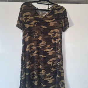Camouflage kortklänning med v-ringning - Säljer en cool kortklänning med klassiskt camouflage-mönster i bruna och beige toner. Klänningen har v-ringad hals och korta ärmar, perfekt för dig som gillar streetstyle och vill sticka ut. Materialet känns mjukt och skönt mot huden.