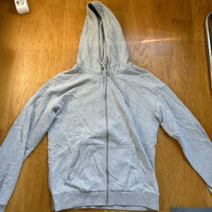 Grå hoodie från Even&Odd med dragkedja - Säljer en enkel och snygg grå hoodie från Even&Odd. Tröjan har huva med snörning, hel dragkedja framtill och fickor. Tillverkad i mjuk bomullsmix, perfekt för chill dagar eller när du vill vara bekväm. Långärmad och klassisk passform.