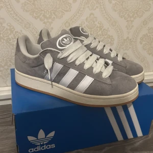 Adidas Campus 00S grå sneakers - Tja, säljer mina gråa Adidas Campus 00S, varför jag säljer dom är för att jag inte tycker dom passar min stil väldigt bra! Köpte dom denna sommar och inte använt dom så mycket, skulle nog säga att jag använt dom runt 10 gånger sen jag köpte dom. Dom är i jättefint skick och så är jag väldigt generös med priset! Pris går att diskuteras!