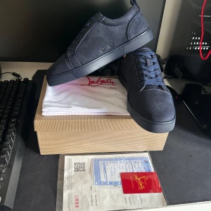 Mörkblå sneakers från Louboutin - Snygga mörkblå sneakers från Louboutin i mocka med klassisk röd sula och broderad logga på hälen. Skorna har rund tå, platt sula och snörning. Perfekta för dig som vill sticka ut med exklusiva detaljer och lyxig känsla.