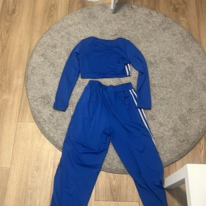 Blå croppad långärmad topp Shein - Säljer en blå croppad långärmad topp från Shein med vita ränder längs ärmarna. Toppen har en sportig vibe och är tillverkad i ett stretchigt syntetmaterial som passar perfekt till träning eller chill. Matcha med byxor för en komplett look!