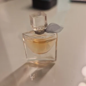 Elegant parfymflaska med rosett - Stilren parfymflaska med en dekorativ rosett vid halsen. Perfekt för dig som vill ha en snygg detalj på sminkbordet. Volym, ingredienser och tillverkningsland kan ej utläsas från bilden. Vet ej vilket märke ganska mycke kvar 85% liten flaska 10 ml tror jag