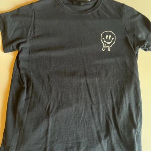 Svart t-shirt CREATE från Lager157 - Svart t-shirt från 157 med coolt tryck av ett smält smiley-ansikte på bröstet och stor text 'CREATE' på ryggen. Klassisk rund hals och korta ärmar. Skön och mjuk i bomull, perfekt för en kreativ vibe.