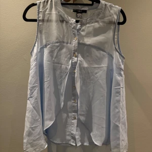 Ljusblå ärmlös blus från Ellos - Säljer en ljusblå ärmlös blus från Ellos med rund halsringning och knäppning framtill med små knappar. Blusen har en lös passform och är tillverkad i ett lätt, mjukt tyg som ger en luftig känsla. Perfekt för alla tillfällen och enkel att styla.