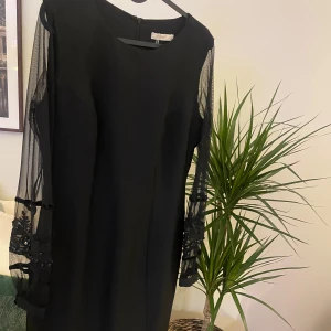 Svart klänning med meshärmar och broderi - Svart ny och inte använt klänning. Ärmarna har broderade detaljer och pärlor som ger en extra touch. Klänningen har rund halsringning och dragkedja bak. 🩷
