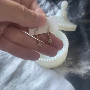 Guldiga örhängen med små stjärnor/ 18 k guldpläterade  - Supersöta guldiga örhängen med små hängande stjärnor dekorerade med vita stenar.  Köpta i Turkiet ! Perfekta för att ge din look lite extra bling. Smidig klickstängning och nätta detaljer som passar till många stilar.