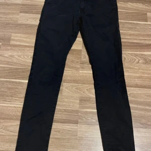 Svarta byxor från Jack & Jones - Svarta byxor från Jack & Jones i slim fit-modell. Byxorna har klassisk design med fickor fram och bak, bälteshällor och knappgylf. Perfekta för en clean och stilren look. Materialet är mjukt och bekvämt, passar till många olika outfits.