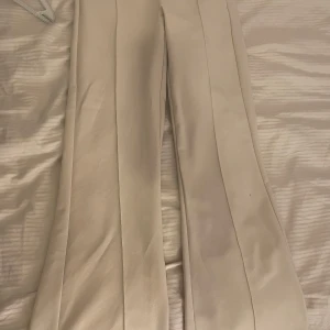 Beiga kostymbyxor från Gina Tricot XS - Snygga beiga kostymbyxor från Gina Tricot i storlek XS. Byxorna har raka ben, pressveck framtill och dold dragkedja med hake i midjan. Perfekt för en clean och stilren look. Materialet känns mjukt och har en lätt struktur.