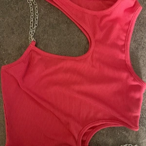 Rosa ribbad magtröja med kedjedetalj - Snygg rosa magtröja med ribbad struktur. Ena axelbandet är ersatt med en  silverfärgad kedja. Och en kedja vid midjan. 