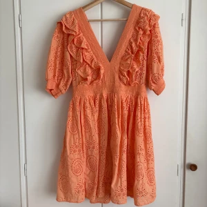 Persikofärgad klänning med volanger H&M - Snygg persikofärgad kortklänning från H&M med broderade detaljer och volanger längs den djupa v-ringningen. Klänningen har puffiga kortärmar och dragkedja i ryggen. Storlek 42, men passar typ mig som har S/M i vanliga fall (beroende på hur man vill att den ska sitta)🧡