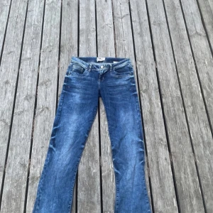 Blå bootcut jeans med råa kanter - Snygga blå jeans med bootcut passform och råa, fransiga kanter nertill. Klassisk femficksmodell med ljus tvätt och diskreta slitningar. Jeansen har normal midja och är tillverkade i klassiskt denimtyg. Perfekta för en avslappnad och trendig look.