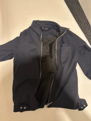 Mörkblå jacka från Jack&jones Premium M - Mörkblå jacka från JAPANONES Premium i storlek M. Jackan har klassisk krage, dragkedja framtill och knappdetaljer vid ärmslut och midja. Snygg och stilren modell som passar perfekt till många olika outfits.nypris 1500