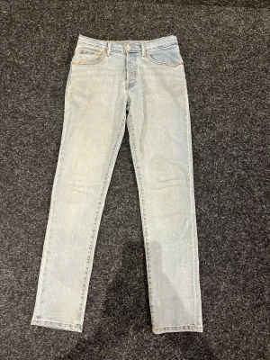 Levi's 501 ljusa jeans straight fit - Säljer ett par klassiska Levi's 501 jeans i ljusblå tvätt med raka ben och normal passform. Jeansen har fem fickor, knappgylf och snygga kontrastsömmar. Perfekt för dig som gillar tidlös stil och vill ha ett par jeans som funkar till allt.