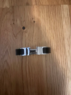 H Armband 17cm - Snyggt armband från H i silverfärgad metall med svart emalj och ikoniskt H-spänne. Stilren och modern design som ger en lyxig känsla till din outfit. Perfekt accessoar för dig som gillar exklusiva detaljer.