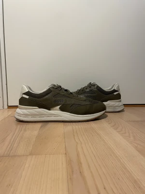 Olivgröna sneakers från Hugo Boss - Snygga sneakers från Hugo Bossi olivgrönt med vita och bruna detaljer. Skorna har en blandning av mocka och mesh, vit sula med BOSS-logga runtom och snörning. Perfekta för dig som gillar stilrena och sportiga vibes.