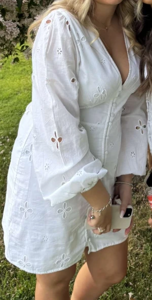 Vit broderad student klänning från NA-KD  - Superfin vit kortklänning från NA-KD med broderade blommor, v-ringning och knappar framtill. Långa ärmar med lätt puff och resår vid handlederna. Perfekt för sommarens alla tillfällen, i luftig bomull som känns fräsch och lätt. Storlek L men jätte liten i storleken passar S/M. Perfekt student klänning🥹