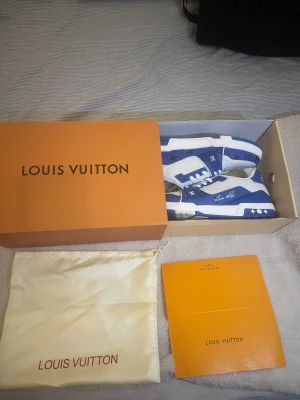 Louis Vuitton blå/vita sneakers - Exklusiva Louis Vuitton sneakers i blått och vitt med #54 på hälen och tydliga LV-loggor. Skorna har snörning, platt sula och rund tå. Materialet är skinn med präglade monogramdetaljer och kontrasterande blå paneler. Snygg design med box och dustbag medföljer.