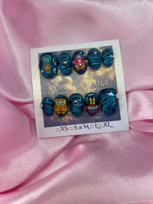 SpongeFriends (M);ExtraShortOval  - Unika press-on naglar i storlek M: 16 mm, 12 mm, 12,5 mm, 11,5 mm, 10 mm med cateye metallic blå bas och  3D-motiv av Svampbob, Patrick, Bläckvard och Herr Krabba. Naglarna har extra kort oval form och dekorerade detaljer med kristaller. Perfekt för dig som vill ha färgglada och roliga naglar.