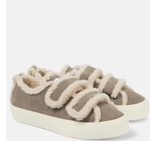 Fluffiga Skor - Unika sneakers med mjuka fårskinnsdetaljer och breda kardborreband. Finns i beige, svart, brun och vinröd mocka med kontrasterande vit eller brun sula. Rund tå och platt sula ger en chill vibe, perfekt för dig som gillar statement-skor med cozy känsla.