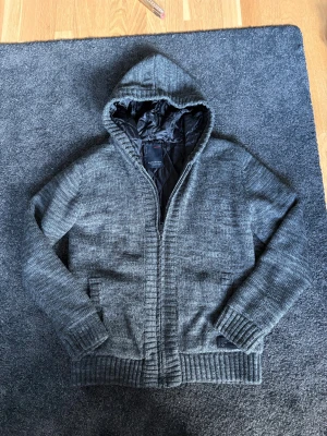 Fodrad cardigan - Stickad fodrad cardigan från Reserved i storlek M. Jackan har quiltat svart foder, dragkedja framtill och två fickor. Ribbad kant vid ärmslut och nederkant ger en schysst look. Perfekt för dig som gillar chill och enkel stil.