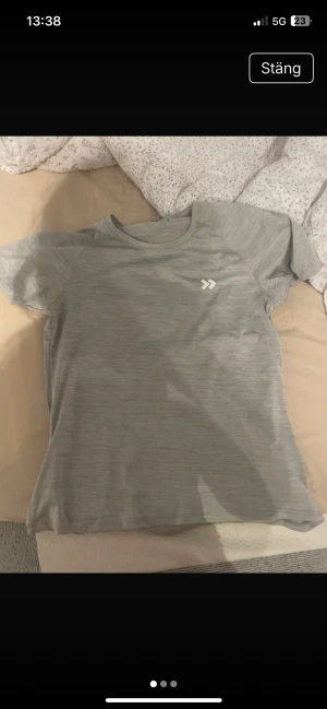 Grå tränings-tshirt från 157 - Snygg grå t-shirt från 157 med diskret mönster och logga på bröstet. Perfekt för träning, med korta ärmar och rund hals. Materialet är lätt och andas, vilket gör den skön att ha på sig under aktiva dagar.