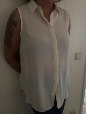 Vit ärmlös skjorta med krage - Snygg vit skjorta i tunn och lätt polyester med klassisk krage och knappar framtill. Modellen är ärmlös och har en rak passform som ger en clean och fräsch look. Från HMs tidigare sortiment, finns ej att köpa längre. Aldrig använd