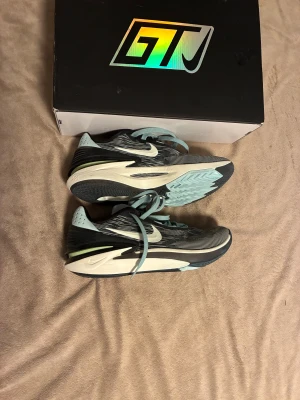 Nike GT Cut 2 sneakers svart/blå - Nike GT Cut 2 sneakers i svart, ljusblått och vitt med coola mönster på ovandelen. Skorna har snörning, platt sula och tydlig Zoom Air-dämpning. Perfekta för dig som vill ha snygga och sportiga skor med modern design och grym komfort.