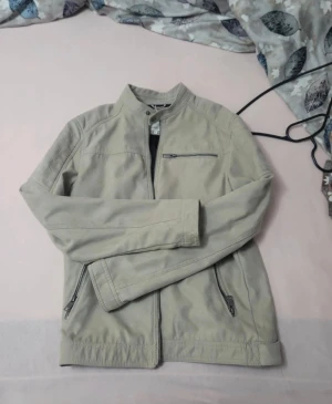 Beige bomberjacka med dragkedjor - Stilren beige bomberjacka från Jack & Jones med ståkrage och tre dragkedjefickor. Jackan har slät yta, fodrad insida och raka ärmar. Perfekt för dig som gillar en clean look och vill ha en jacka som funkar till många outfits. Använt 2 gånger max och inga täcken på användning.