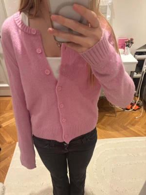 Rosa kofta från Zara - Säljer en söt rosa kofta med rund hals och matchande rosa knappar. Koftan har långa ärmar och ribbade muddar vid ärmslut och nederkant. Perfekt att slänga över en topp för en chill och färgglad look.